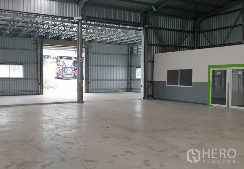 Warehouse for rent in Pak Kret, Nonthaburi - Interior view toward wide loading doors with natural light and an adjacent office unit.