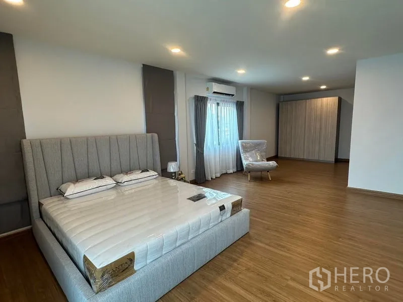 Detached House for rent in Bang Phli, Samut Prakan - Spacious master bedroom with upholstered bed, wood floors, wardrobe and lounge chair.
