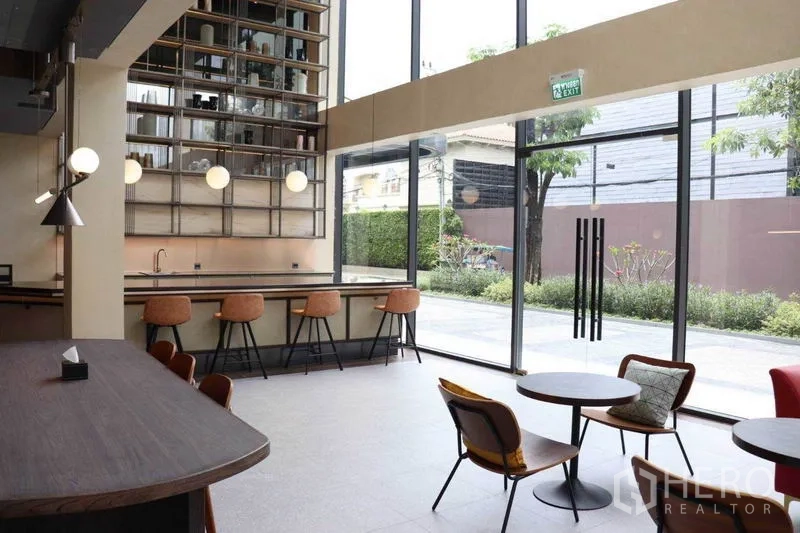 零售空间 出租在Phra Khanong, Bangkok - 采光充足的零售就座区，圆桌与吧椅，落地玻璃面向绿化步道。