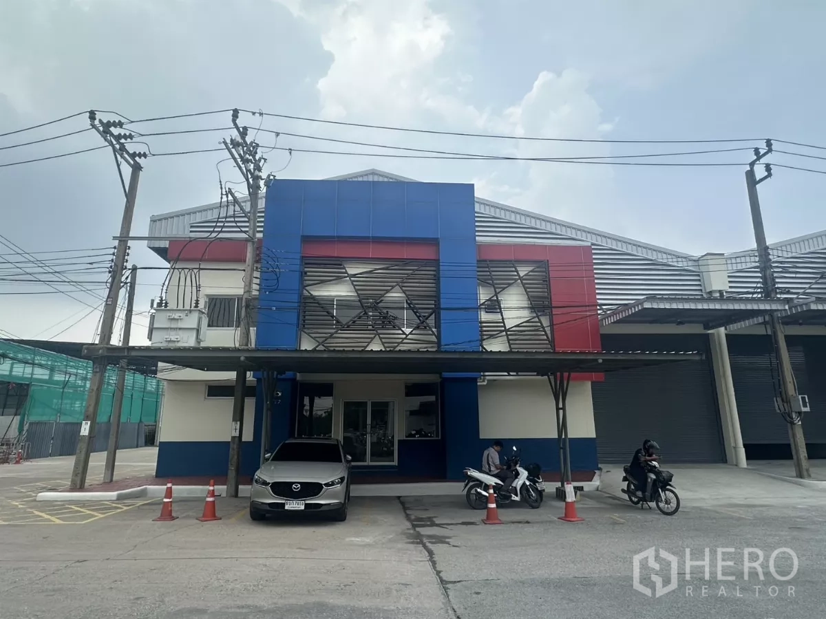 Factory for rent in Bang Phli, Samut Prakan - Modern factory frontage with blue and red panels, covered parking and power lines.