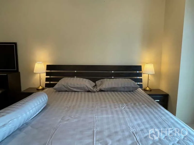 房间 出租在Khlong Toei, Bangkok - 特大床近景，床头柜与暖色台灯