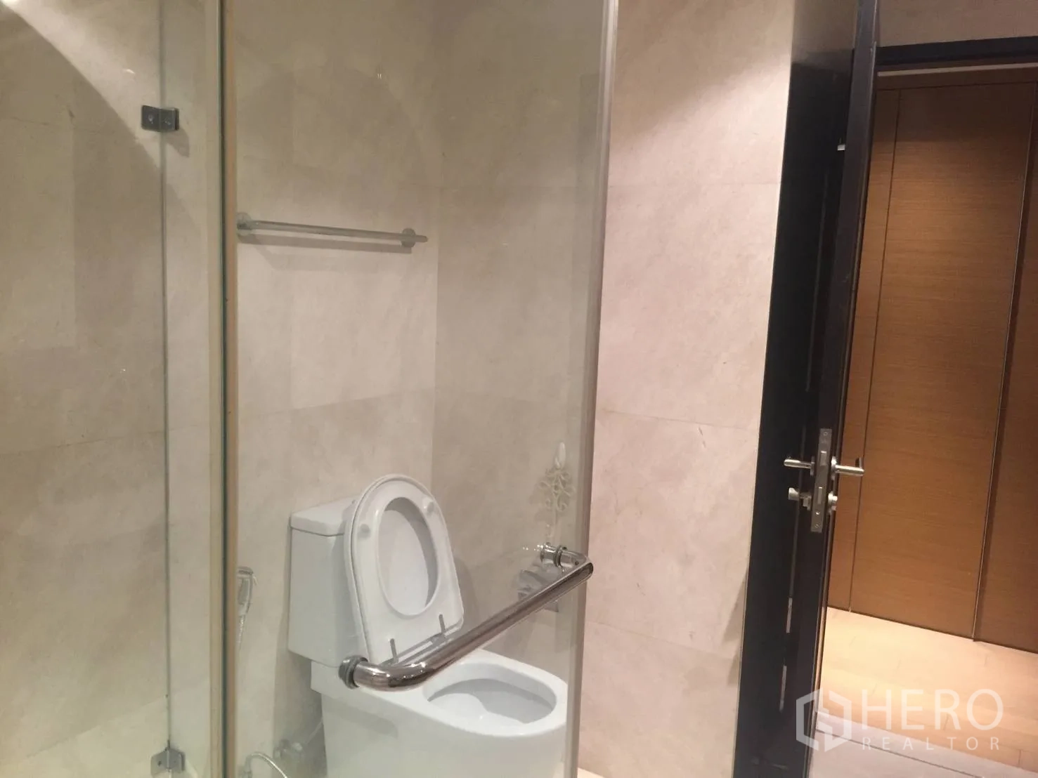 Condominium for rent in Watthana, Bangkok - Guest bathroom with toilet behind a glass partition and beige tiles.