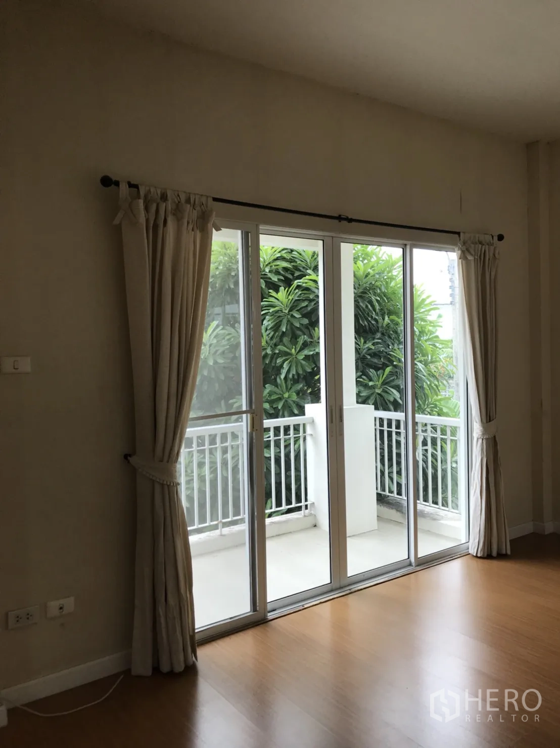 บ้าน ให้เช่าในLat Krabang, Bangkok - ห้องนอนมีประตูกระจกบานเลื่อนไปยังระเบียง มองเห็นต้นไม้และราวระเบียงสีขาว