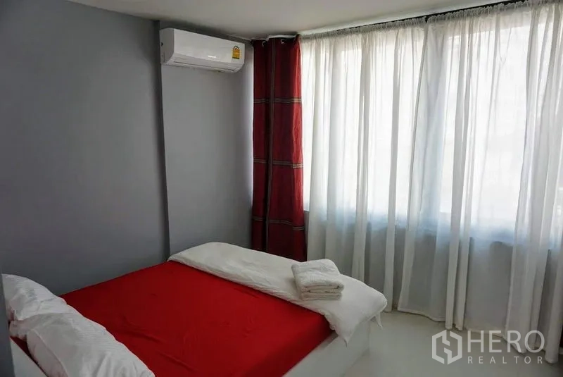 店屋 出售在Phra Khanong, Bangkok - 次卧，红色床品、角落空调与整面采光窗。