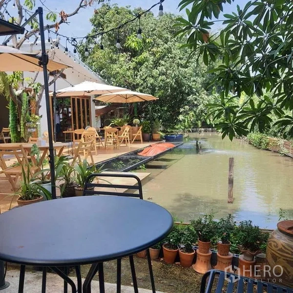 พื้นที่ขายปลีก ให้เช่าในSuan Luang, Bangkok - ที่นั่งเอาท์ดอร์ริมคลอง โต๊ะกลม ร่มสนาม และไฟประดับ ท่ามกลางสวนเขียว