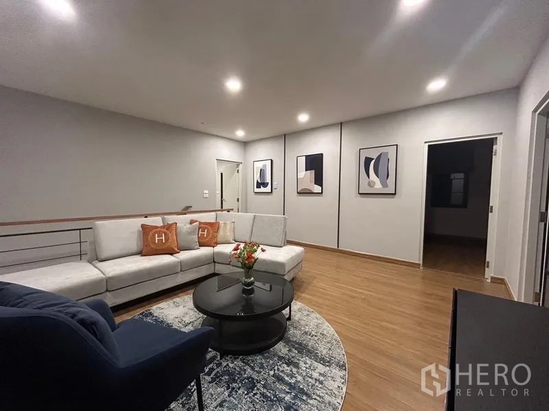 Detached House for rent or sale in Bang Phli, Samut Prakan - Upper‑floor living area with L‑shaped sofa, round rug, coffee table and framed artwork.