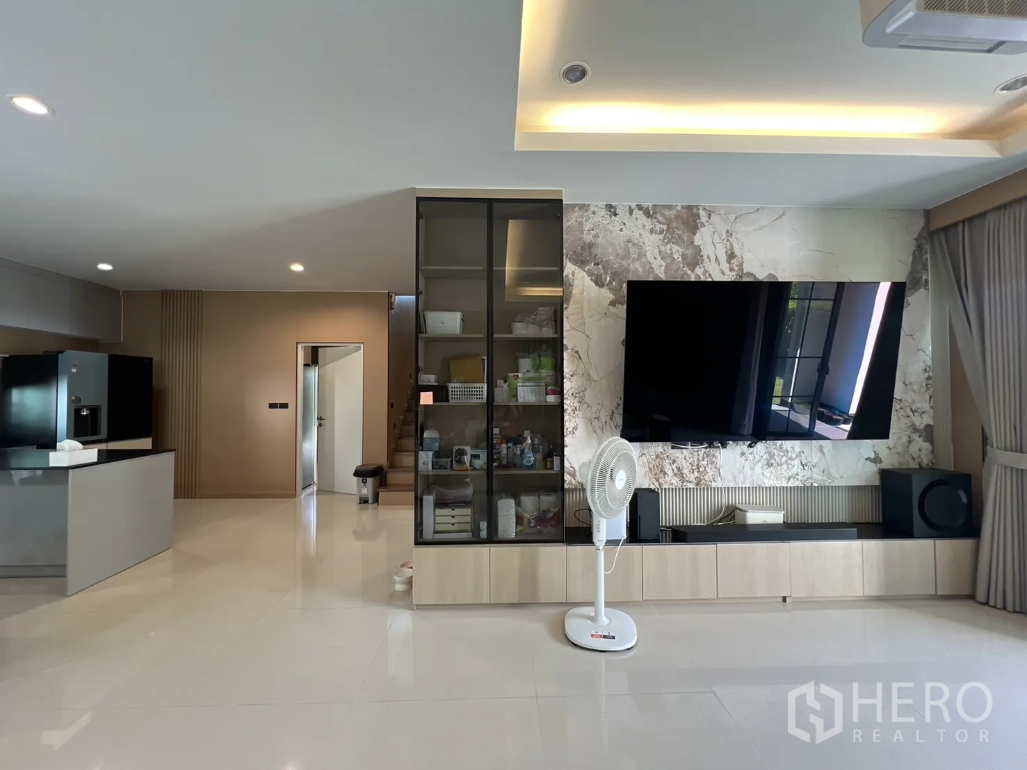 Detached House for rent or sale in Mueang Pathum Thani, Pathum Thani - Open-plan living area showing TV wall, built-in storage and staircase.
