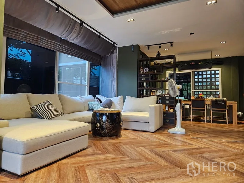 Detached House for sale in Thawi Watthana, Bangkok - Open-plan living area with sectional sofas, bookshelves and wood floors.