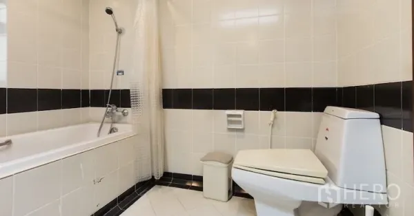 Condominium for rent in Sathon, Bangkok - Second bathroom with white tiles, bathtub and toilet in a clean, simple style.