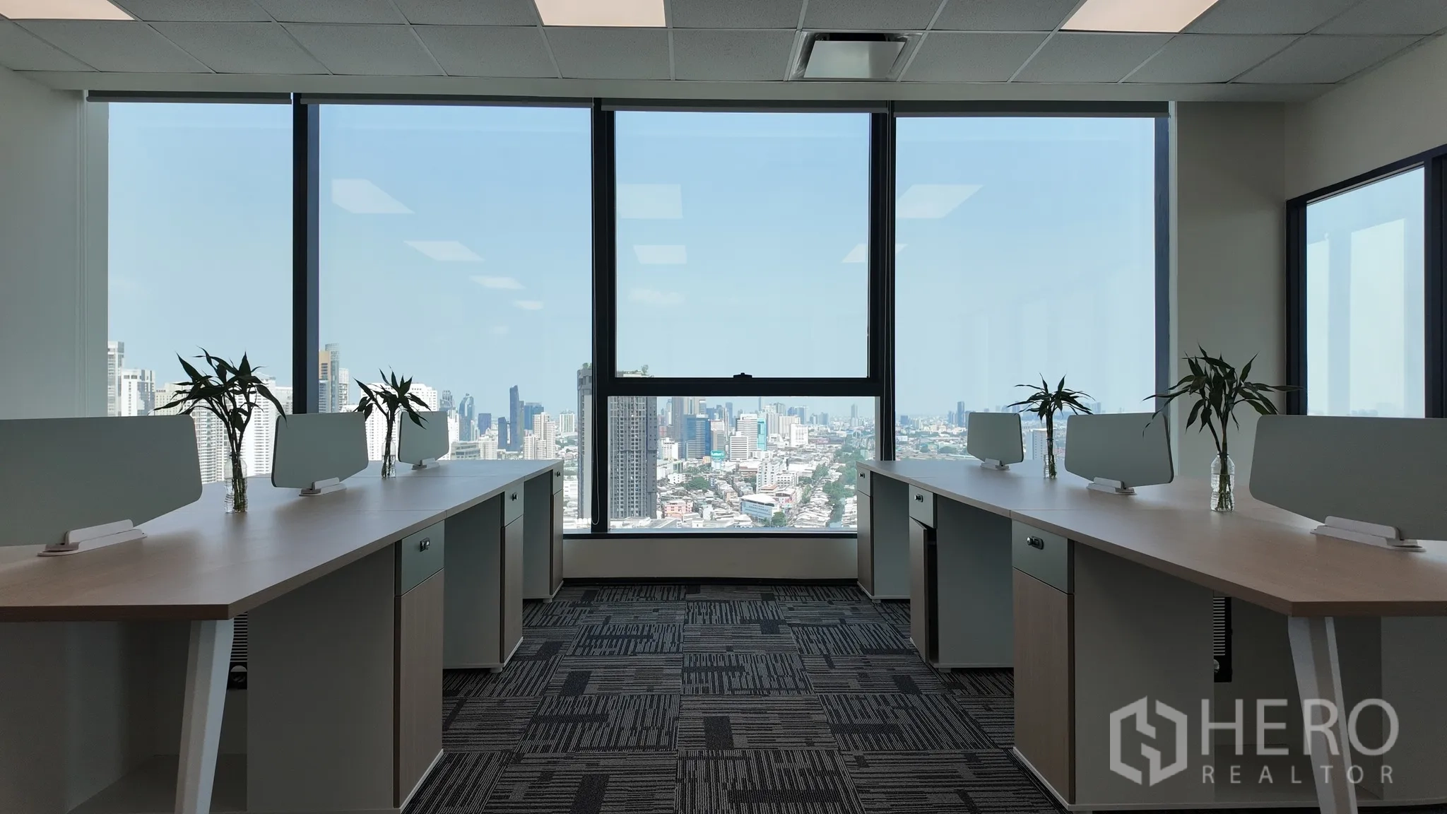 Office Space for rent in Khlong Toei, Bangkok - Open-plan office with long desks and dividers facing large windows and a city skyline view.