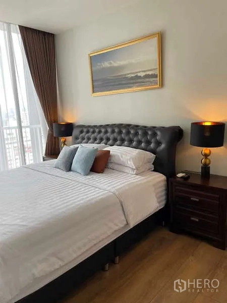 Condominium for rent or sale - Primary bedroom with tufted headboard bed, bedside tables with lamps and large window with curtains.