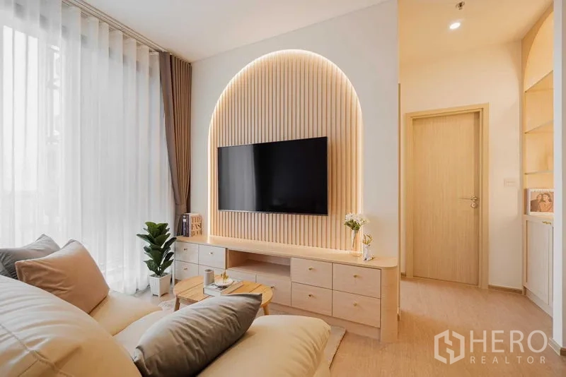 Condominium for rent in Watthana, Bangkok - Bright living room with sofa facing arched TV wall and large windows.
