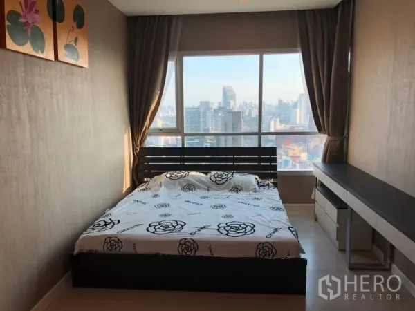 Condominium for rent or sale in Huai Khwang, Bangkok - Master bedroom with floor-to-ceiling windows showcasing a panoramic Bangkok skyline.