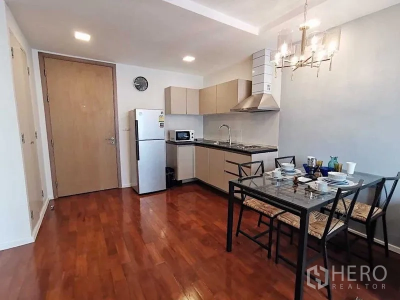 Condominium for sale in Khlong Toei, Bangkok - L-shaped kitchen with stainless fridge, range hood, and four-seat dining table.