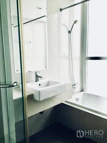 Condominium for rent in Watthana, Bangkok - Bathroom with bathtub beside a large window and a white vanity.