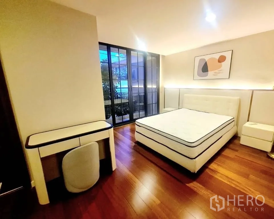 Townhouse for rent or sale in Watthana, Bangkok - Bedroom with work desk and sliding glass doors opening to the balcony.
