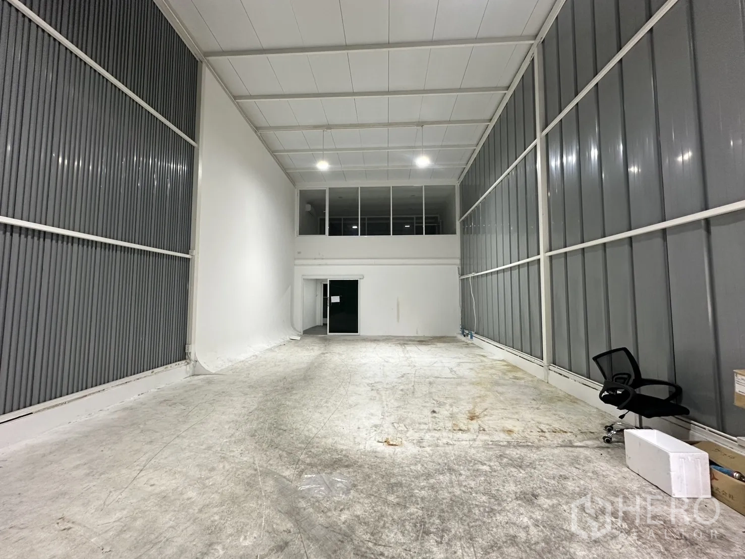 Warehouse for rent in Suan Luang, Bangkok - High‑ceiling warehouse hall with metal side walls, bright lighting and a mezzanine office at the rear.