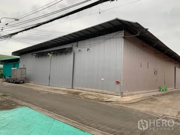 货栈 出租在Bang Kapi, Bangkok - 金属外墙仓库外观，宽大推拉门，车辆可通行的铺装车道，位于曼谷 Bang Kapi。