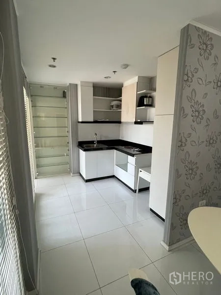 Condominium for sale in Suan Luang, Bangkok - Light-filled galley kitchen with L-shaped counters, glass shelving and window blinds.