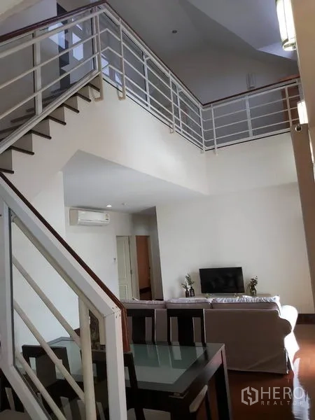 公寓 出租在Watthana, Bangkok - 挑高客厅配金属楼梯，沙发位于夹层下方。