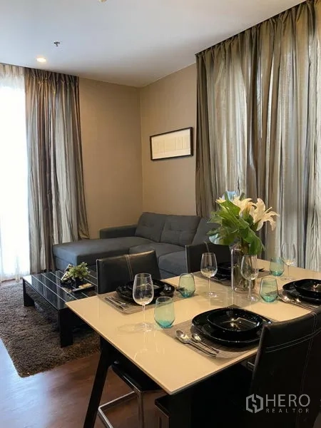 公寓 出租在Watthana, Bangkok - 四人餐区毗邻灰色转角沙发与茶几，高窗纱帘引入自然光。