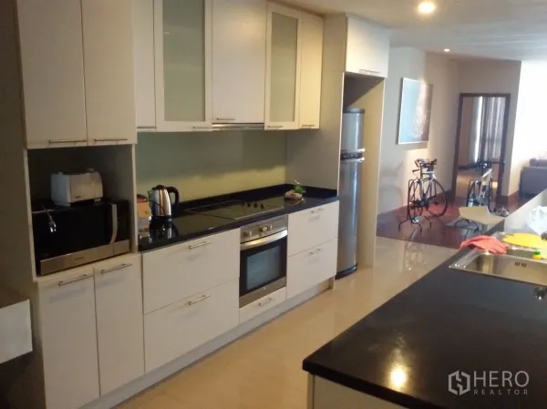Condominium for rent in Sathon, Bangkok - Open-plan kitchen with white cabinetry, built-in oven, cooktop and black granite countertop.