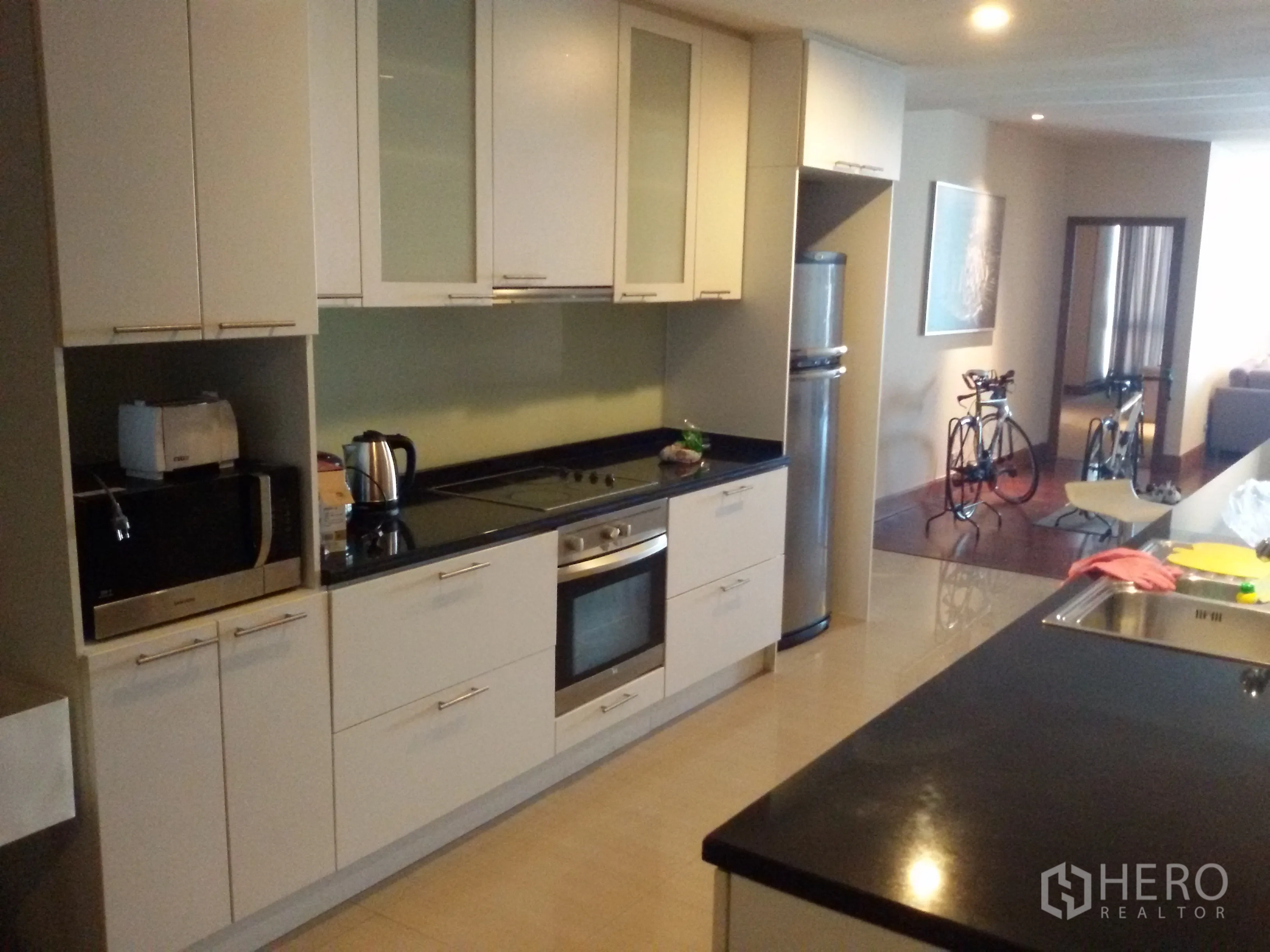 Condominium for rent in Sathon, Bangkok - Open-plan kitchen with white cabinetry, built-in oven, cooktop and black granite countertop.