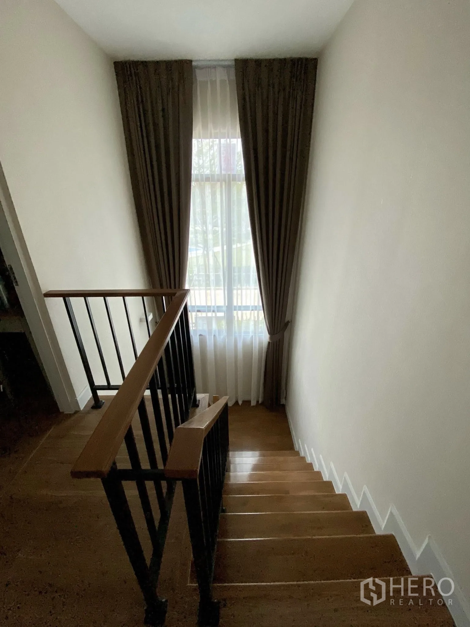 Detached House for sale in Saphan Sung, Bangkok - Wood staircase with black metal balustrade and a tall curtained window.