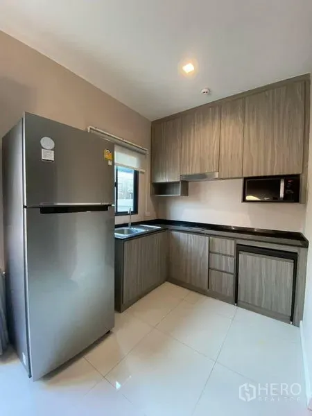 Townhouse for rent - Compact L-shaped kitchen with wood-grain cabinets, black countertops, sink and stainless-steel fridge.