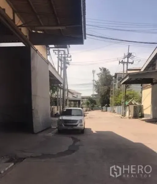 Warehouse for rent in Chachoengsao - Wide driveway between warehouse buildings with utility poles and parking, suitable for truck access.