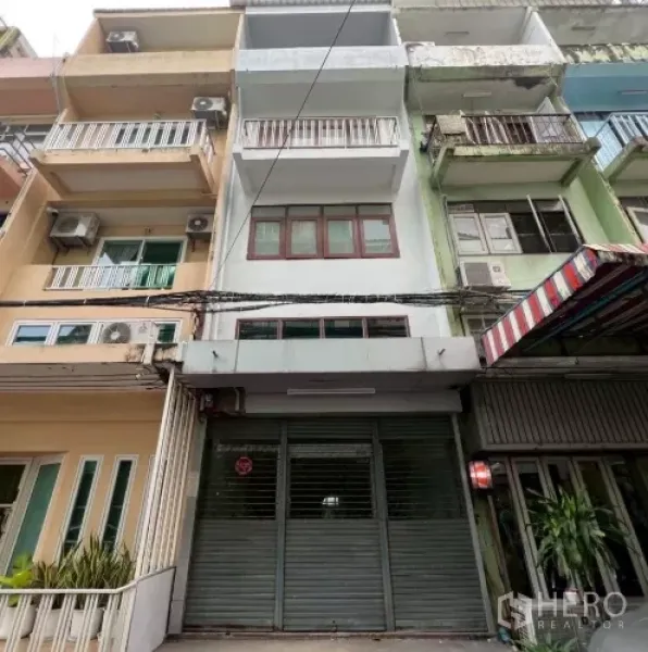 อาคารพาณิชย์ ให้เช่าในKhlong Toei, Bangkok - ด้านหน้าอาคารพาณิชย์พร้อมประตูม้วนโลหะและระเบียงในย่านเมือง.