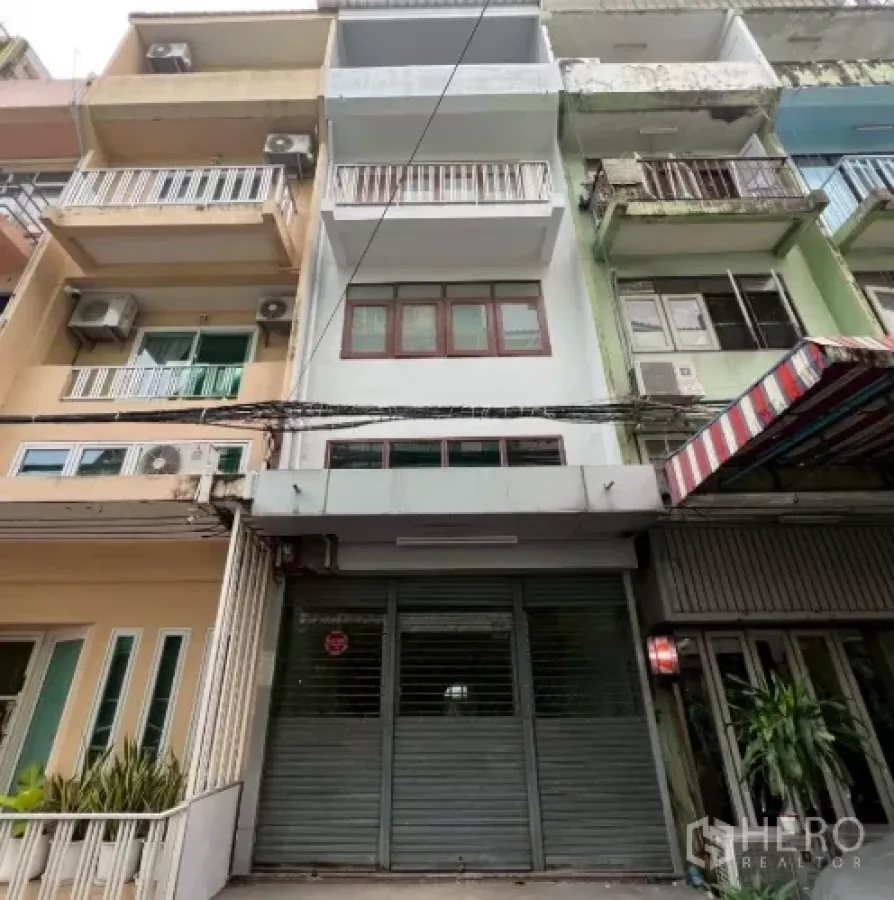 อาคารพาณิชย์ ให้เช่าในKhlong Toei, Bangkok - ด้านหน้าอาคารพาณิชย์พร้อมประตูม้วนโลหะและระเบียงในย่านเมือง.