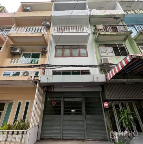 อาคารพาณิชย์ ให้เช่าในKhlong Toei, Bangkok - ด้านหน้าอาคารพาณิชย์พร้อมประตูม้วนโลหะและระเบียงในย่านเมือง.