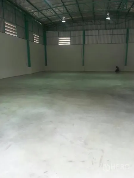 Warehouse for rent in Pathum Thani - Empty warehouse hall showing heavy-duty concrete slab floor, green steel frames and ventilated side windows.