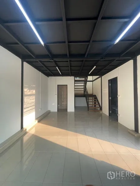 Warehouse for rent in Bang Kapi, Bangkok - Ground-floor office area with tiled floors, black grid ceiling and staircase connection.