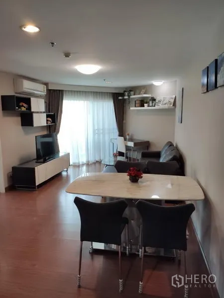 Condominium for rent in Huai Khwang, Bangkok - Open-plan living and dining area with TV console, marble-top table and balcony access.