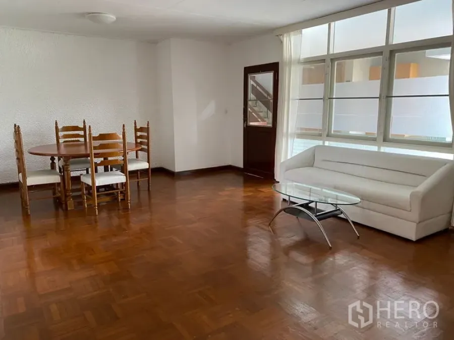 Apartment for rent in Khlong Toei, Bangkok - Spacious living and dining area with parquet floors, white sofa, glass coffee table and large windows.