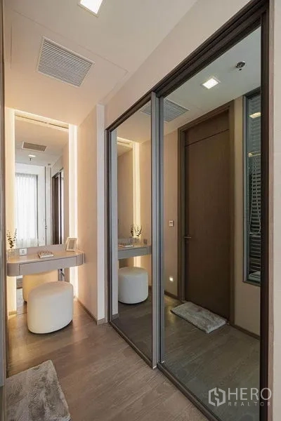 Condominium for rent in Watthana, Bangkok - Hallway with mirrored sliding wardrobe and a lighted vanity desk with stool.