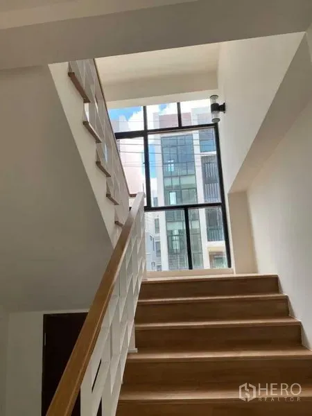 Home Office for rent or sale in Bang Phli, Samut Prakan - Bright stairwell with wooden steps and a tall window bringing natural light into the home office.