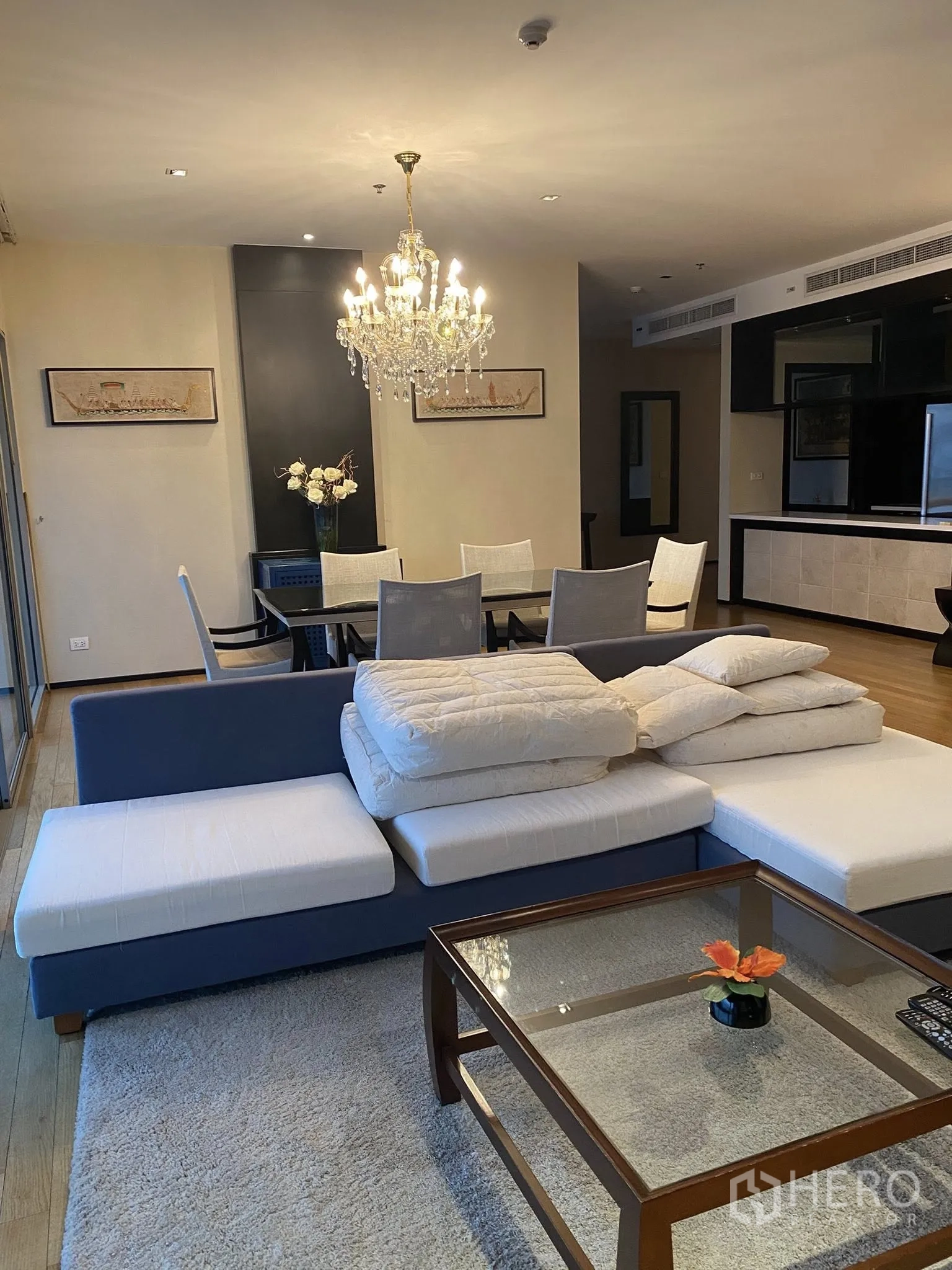Condominium for rent in Watthana, Bangkok - Open-plan living and dining area with chandelier, blue-and-white sofa, glass coffee table, and wood flooring.