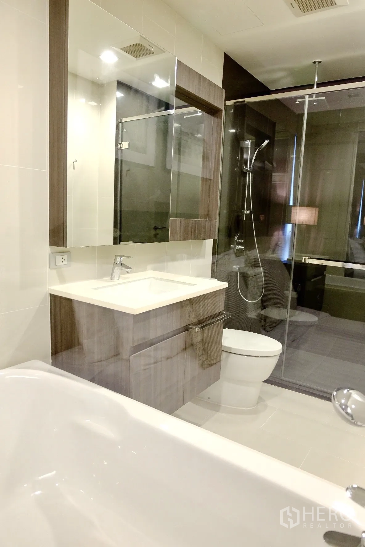 Condominium for rent in Watthana, Bangkok - Modern bathroom with bathtub, vanity cabinet, and separate glass shower enclosure.