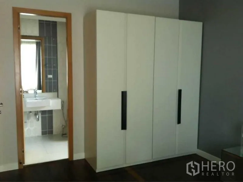 公寓 出售在Ratchathewi, Bangkok - 卧室配大白色衣柜，门通向带现代洗手台和灰色瓷砖的套内卫浴。