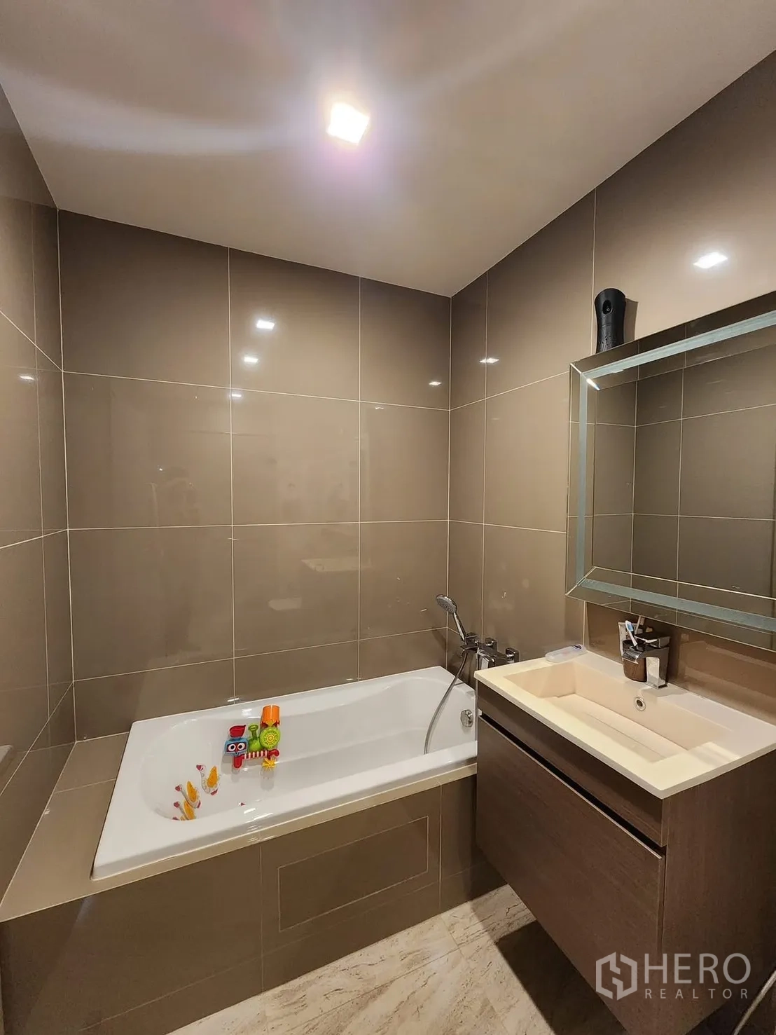 Condominium for rent in Watthana, Bangkok - Bathroom with built-in soaking bathtub, vanity cabinet, and wall mirror in neutral tiles.