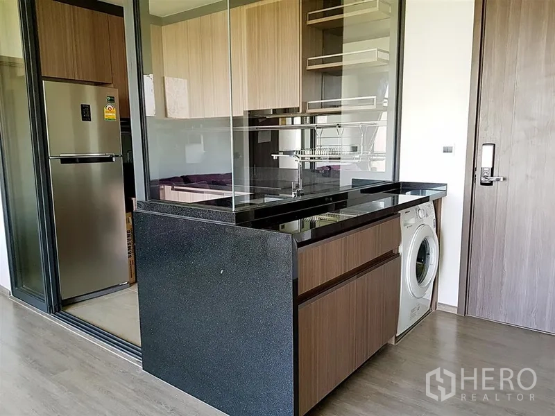 Condominium for rent in Watthana, Bangkok - Kitchen island with black stone countertop and in-unit washing machine.