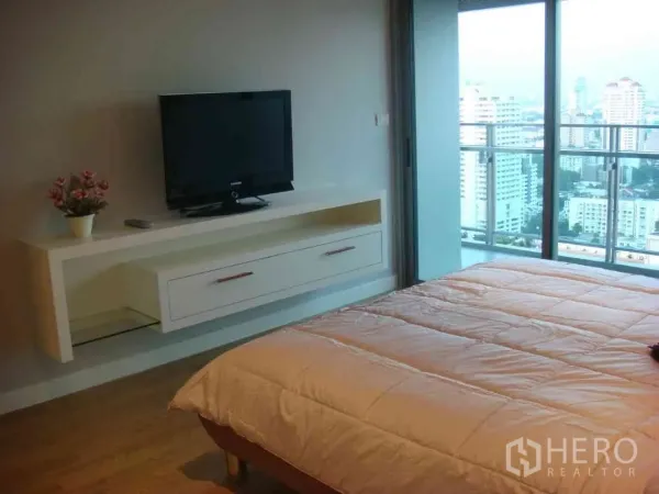 Condominium for rent in Watthana, Bangkok - Master bedroom with TV console opening to a balcony overlooking the Bangkok skyline.