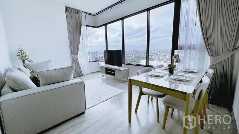 Condominium for rent in Watthana, Bangkok - Bright corner living and dining area with floor‑to‑ceiling windows, TV console, and skyline views over Bangkok.