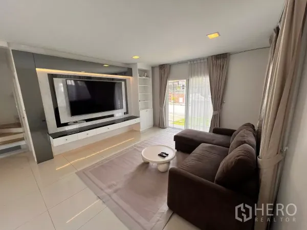 บ้าน ให้เช่าในLat Krabang, Bangkok - ห้องนั่งเล่นโปร่งสว่าง โซฟาตัวแอล ประตูบานเลื่อนกระจก และผนังทีวีบิวท์อิน