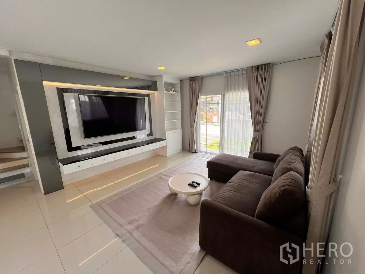 บ้าน ให้เช่าในLat Krabang, Bangkok - ห้องนั่งเล่นโปร่งสว่าง โซฟาตัวแอล ประตูบานเลื่อนกระจก และผนังทีวีบิวท์อิน