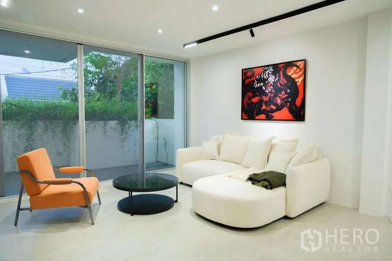 Home Office for rent in Phra Khanong, Bangkok - Cozy living area with white sectional sofa, orange armchair, coffee table and balcony greenery.