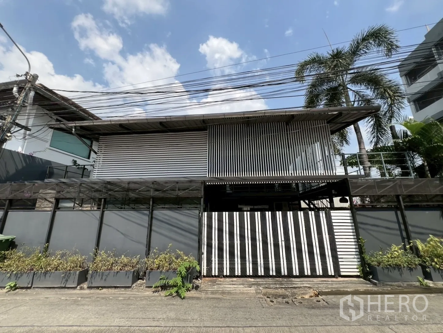 Detached House for rent or sale in Wang Thonglang, Bangkok - Gated two‑storey detached house with corrugated metal facade and privacy slats under a blue Bangkok sky.